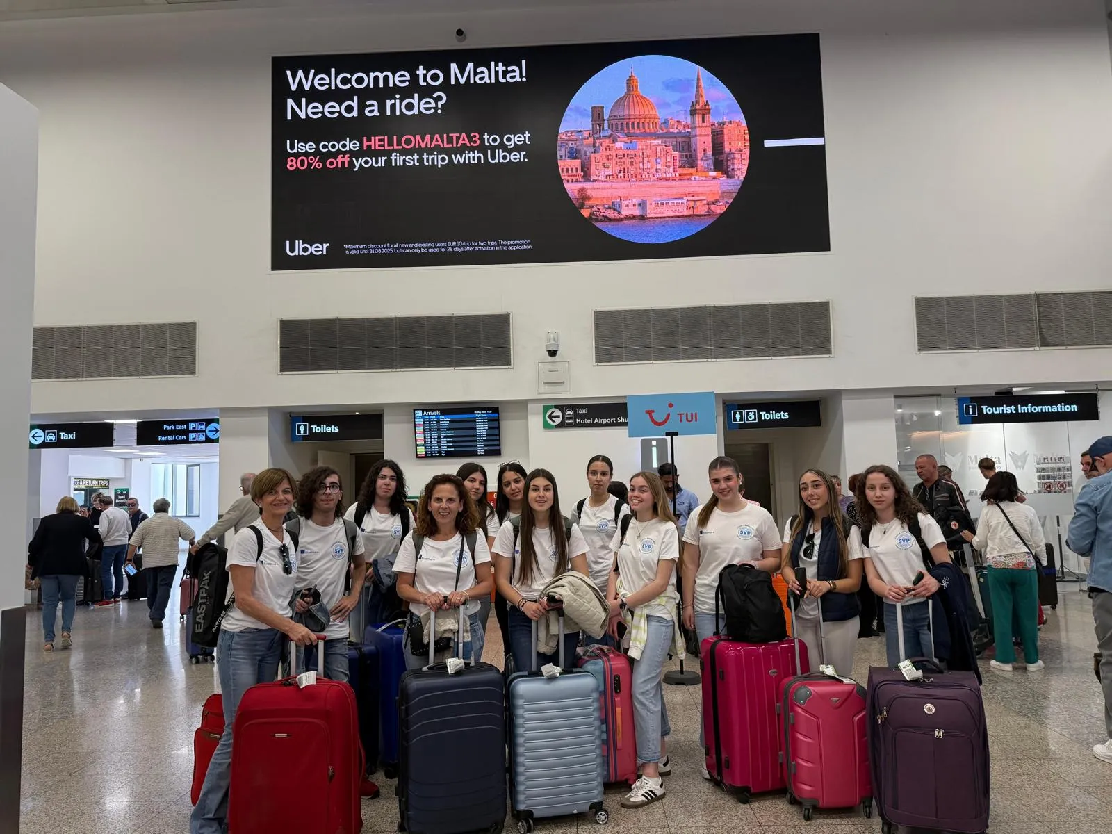Students and teachers with suitcases under the welcome sign at Malta airport